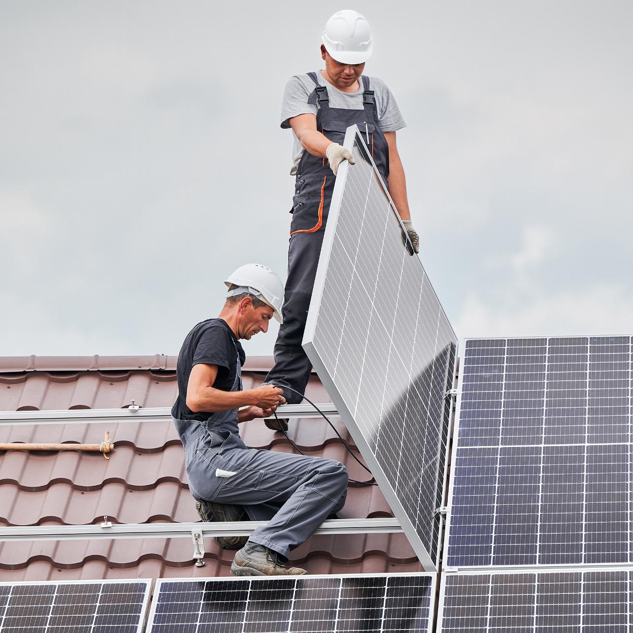 Two workmen adding solar panels to a tiled roof